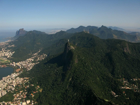 Imagem em vista aérea do Parque Nacional da Tijuca. Na imagem, podemos ver a dimensão da área que o Parque Nacional da Tijuca ocupa em meio à cidade do Rio de Janeiro. No centro da imagem, destaca-se o Morro do Corcovado e o Cristo Redentor. 